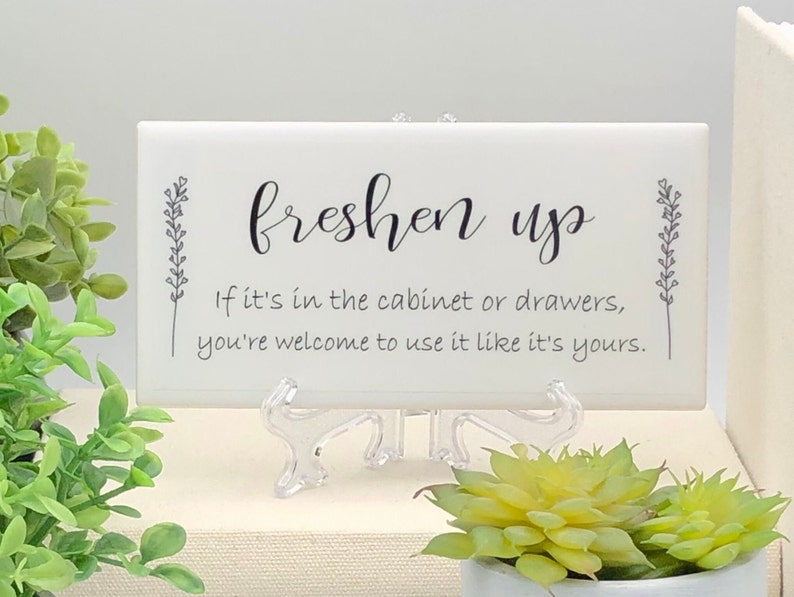 May include: White ceramic sign with black text that reads "freshen up" and "If it's in the cabinet or drawers, you're welcome to use it like it's yours."
