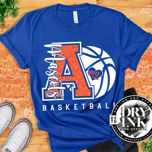 laying flat is a royal blue tshirt by bella and canvas 3001 with a custom glitter basketball mom design in the color glitter ember orange and matte white