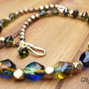 May include: A multi-colored glass bead necklace with gold accents. The necklace features green, blue, and amber glass beads.