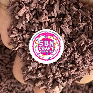 May include: A close-up of a pile of brown chocolate sprinkles. The sprinkles are in a hand, and the background is blurred. The image also includes a logo for "SBN Craft Supplies" with the tagline "Behind your crafts to life one sprinkle at a time."