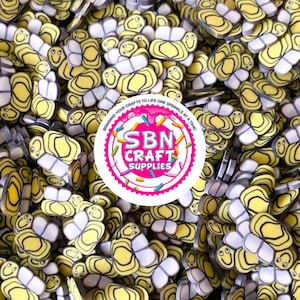 May include: A large quantity of yellow and white butterfly-shaped resin embellishments with black outlines and smiling faces.  The embellishments are scattered on a surface and are perfect for adding a whimsical touch to crafts.