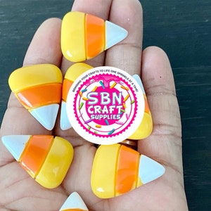 Puede incluir: Un conjunto de suministros para manualidades con forma de caramelos de maíz. Cada pieza presenta la combinación de colores clásica: amarillo, naranja y blanco. La imagen incluye una pegatina redonda con el texto "SBN CRAFT SUPPLIES".