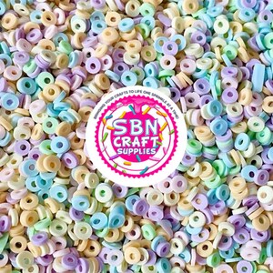Könnte beinhalten: Eine große Menge an pastellfarbenen Donut-Streuseln. Die Streusel haben die Form eines Rings und sind in den Farben Hellblau, Hellgrün, Hellgelb und Helllila.