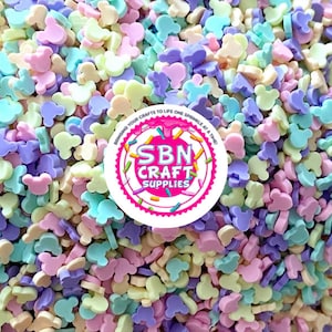 May include: A close-up of a large pile of pastel-colored Mickey Mouse head sprinkles. The sprinkles are in shades of pink, blue, yellow, and purple.