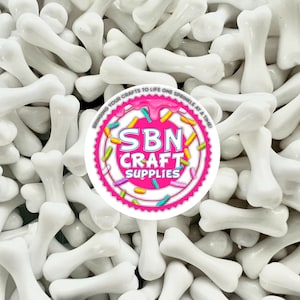 Può includere: Primo piano di decorazioni bianche a forma di osso. Le ossa lucide sono sparse in tutta l'immagine. Un logo circolare con la scritta "SBN CRAFT SUPPLIES" è visibile in alto a destra.