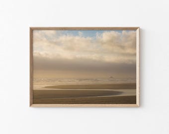 May include: A framed landscape print featuring a beach scene under a cloudy sky. The artwork showcases a sandy beach with gentle waves and a distant landmass. The frame is made of light-colored wood.