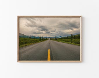 May include: A framed print of a road stretching into the distance under a cloudy sky. The road has a yellow centre line, with green vegetation and mountains visible in the background.