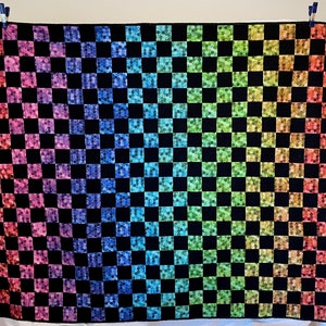 May include: A black and white checkered quilt with a rainbow gradient pattern. The squares are filled with small, colorful dots.
