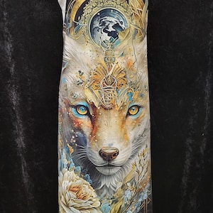 May include: An apron featuring a detailed illustration of a fox with bright yellow eyes, surrounded by floral elements and golden decorative patterns. The design includes a circular celestial motif above the fox head and a large white flower at the base.