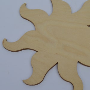 May include: A wooden sun cutout with a light brown colour. The sun has a simple design with eight rays.