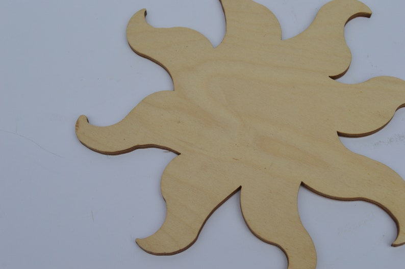 May include: A wooden sun cutout with a light brown colour. The sun has a simple design with eight rays.