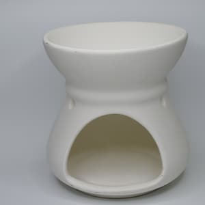 Może przedstawiać: Biały ceramiczny palnik do olejków eterycznych z okrągłym wierzchołkiem i otworem w środku. Palnik jest zaprojektowany do trzymania świeczki typu tealight i małej miseczki na olejki eteryczne.
