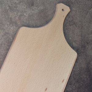 May include: A light brown wooden cutting board with a handle. The board is made of natural wood and has a smooth surface.
