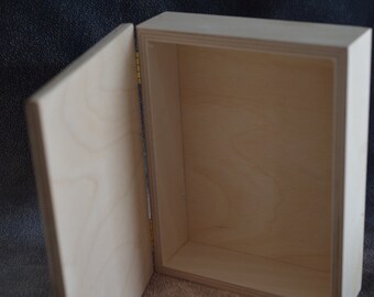 May include: An open, unfinished wooden box with a hinged lid. The box is rectangular with a light wood grain. The lid is partially open, revealing the interior. The box is likely for storage or display.