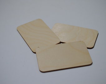 May include: Three unfinished, rectangular wooden tags with rounded corners are arranged on a white surface. The tags have a light, natural wood grain and are suitable for crafting or labeling.