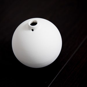 Può includere: Un vaso di ceramica bianca a forma di sfera con un piccolo foro nella parte superiore.