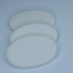 Può includere: Tre sottobicchieri in ceramica di forma ovale bianca. I sottobicchieri sono impilati uno sopra l'altro.