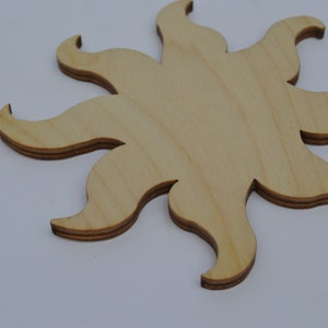 May include: A wooden sun cutout with a light brown colour. The sun has eight points and is made of plywood.