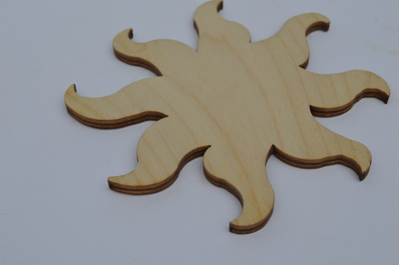 May include: A wooden sun cutout with a light brown colour. The sun has eight points and is made of plywood.