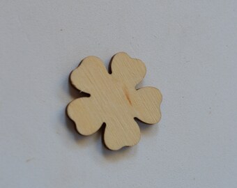 Puede incluir: Un recorte de madera con forma de trébol de cuatro hojas, con un acabado natural de vetas de madera. El trébol está centrado en una superficie blanca, mostrando su forma y textura detalladas. Ideal para manualidades o decoración.