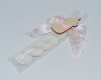 Könnte beinhalten: Eine durchsichtige Plastiktüte gefüllt mit weißen mandelförmigen Bonbons, gebunden mit einem rosa Band mit weißen Punkten und einem Holz-Babyflaschen-Anhänger.