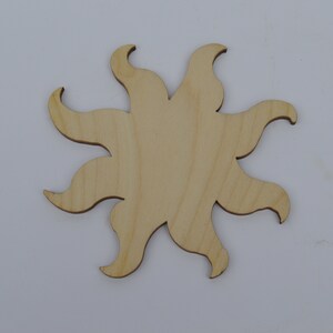 May include: A wooden sun cutout with a simple design. The sun has eight rays that are slightly curved. The cutout is made of light brown wood.