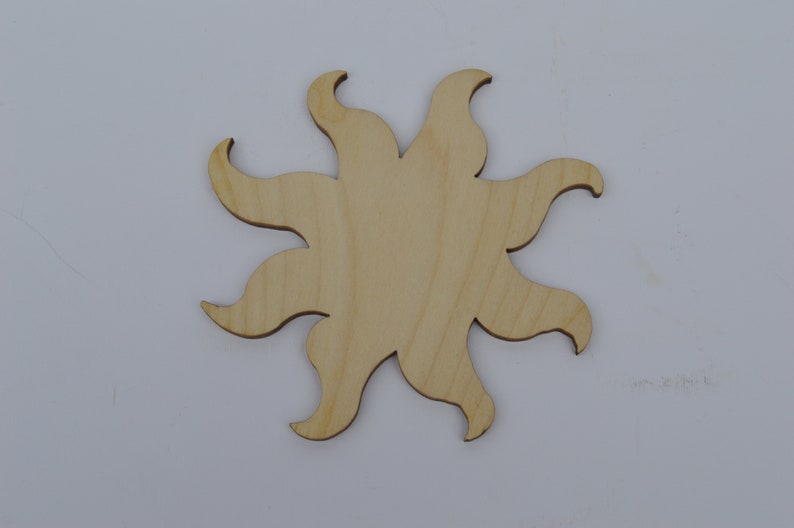 May include: A wooden sun cutout with a simple design. The sun has eight rays that are slightly curved. The cutout is made of light brown wood.