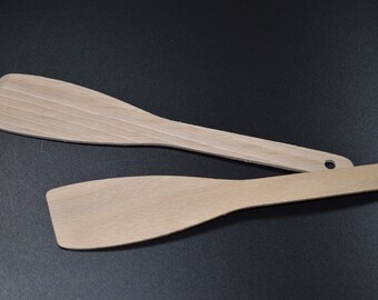 May include: Two wooden spatulas, one on top of the other, on a black surface. The spatulas are light brown and have a smooth, slightly curved surface.