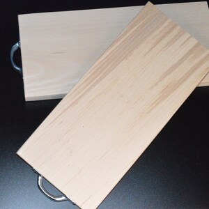 May include: Two wooden cutting boards with metal handles. The boards are light brown and have a natural wood grain.