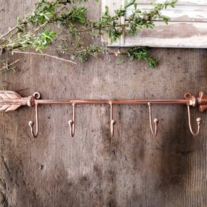Peut inclure: Crochet mural en cuivre en forme de flèche avec cinq crochets. La flèche pointe vers la droite. Le crochet est monté sur un mur en bois.