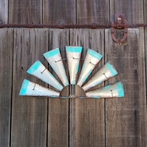 May include: A metal windmill wall decor with a teal blue paint finish. The windmill has 12 blades and is mounted on a wooden wall.