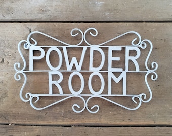 May include: White metal sign with the words "Powder Room" in a decorative script font.
