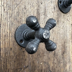 May include: Black cast iron faucet handle wall hook. The hook is shaped like a traditional faucet handle with four knobs.