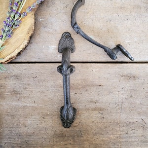 Puede incluir: Dos tiradores de puerta de hierro fundido negro con diseños ornamentados. Los tiradores están sobre una superficie de madera.