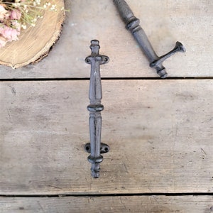May include: Two black cast iron drawer pulls with a decorative design. The pulls are on a wooden surface.