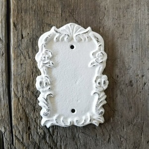 May include: White ceramic light switch cover with a decorative floral design. The cover has a distressed finish and is designed to add a vintage touch to any room.