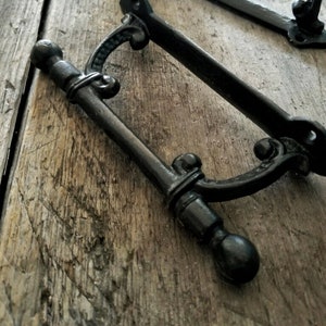 May include: Two black metal door handles with ornate details. The handles have a rounded, decorative end and a curved, open design.