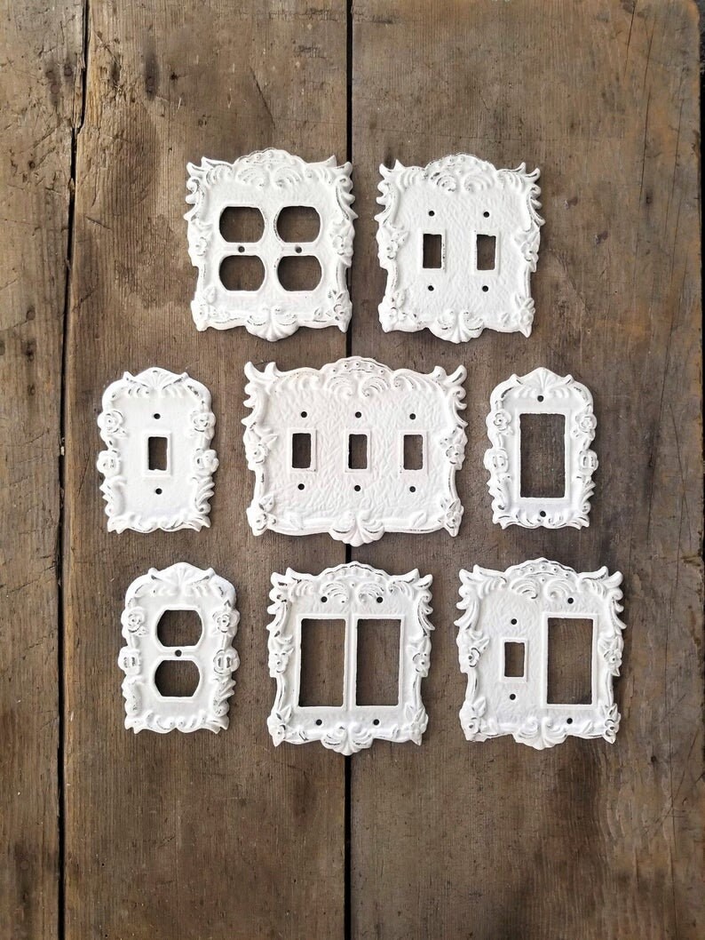 Puede incluir: Conjunto de diez tapas de interruptor de luz decorativas blancas con dise&ntilde;os ornamentados. Las tapas est&aacute;n hechas de hierro fundido y tienen un acabado desgastado.