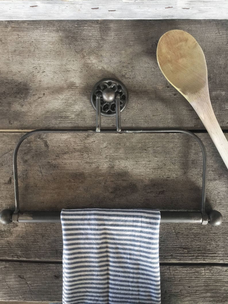 May include: A black metal towel rack with a striped kitchen towel hanging from it. The rack is mounted on a wooden wall.