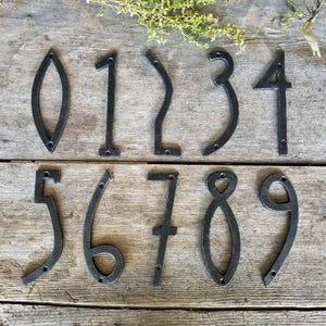 May include: Ten black metal house numbers, 0 through 9, with a unique, modern design. Each number is individually crafted and features a simple, elegant silhouette.