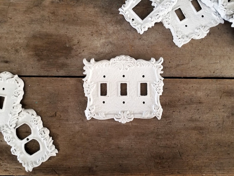 Puede incluir: Tres tapas de interruptor de luz de porcelana blanca con bordes decorativos ornamentados. Las tapas tienen tres y dos interruptores de palanca.