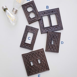 Op de afbeelding: Vijf decoratieve metalen lichtschakelaars in een bruine afwerking. De afdekkingen hebben een ruitpatroon en zijn gelabeld A, B, C, D en E.