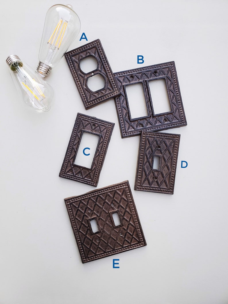 Op de afbeelding: Vijf decoratieve metalen lichtschakelaars in een bruine afwerking. De afdekkingen hebben een ruitpatroon en zijn gelabeld A, B, C, D en E.