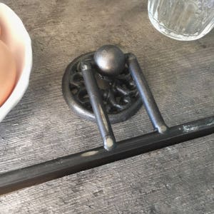May include: A black metal towel rack with a decorative design and a round knob. The rack is mounted on a wooden surface.