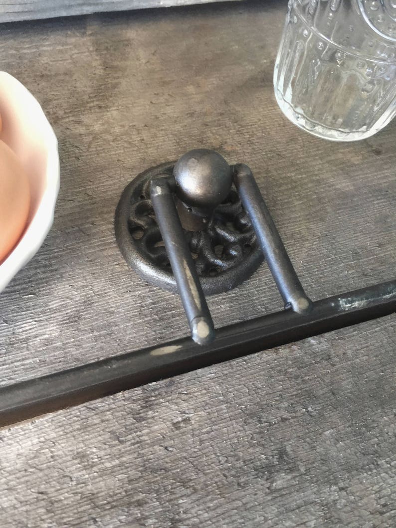 May include: A black metal towel rack with a decorative design and a round knob. The rack is mounted on a wooden surface.