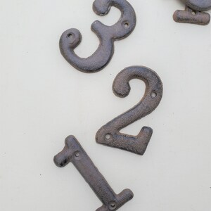 May include: Three cast iron house numbers, 1, 2, and 3, in a dark brown color. The numbers are designed with a rustic, vintage look.