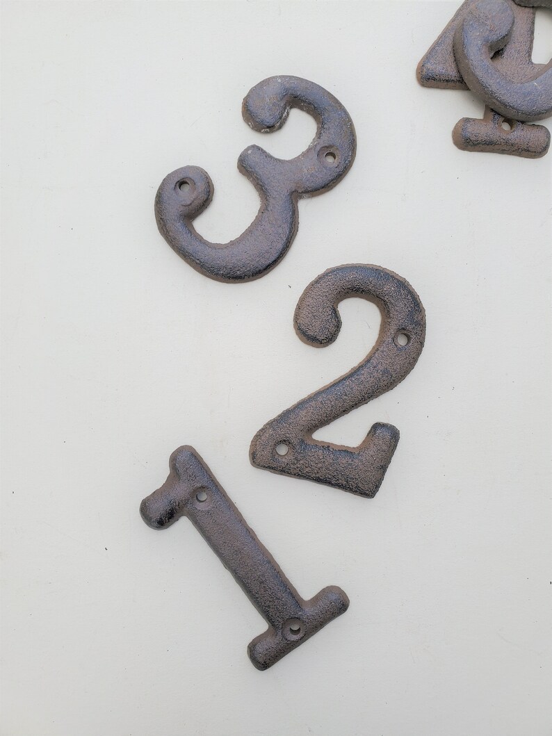 May include: Three cast iron house numbers, 1, 2, and 3, in a dark brown color. The numbers are designed with a rustic, vintage look.