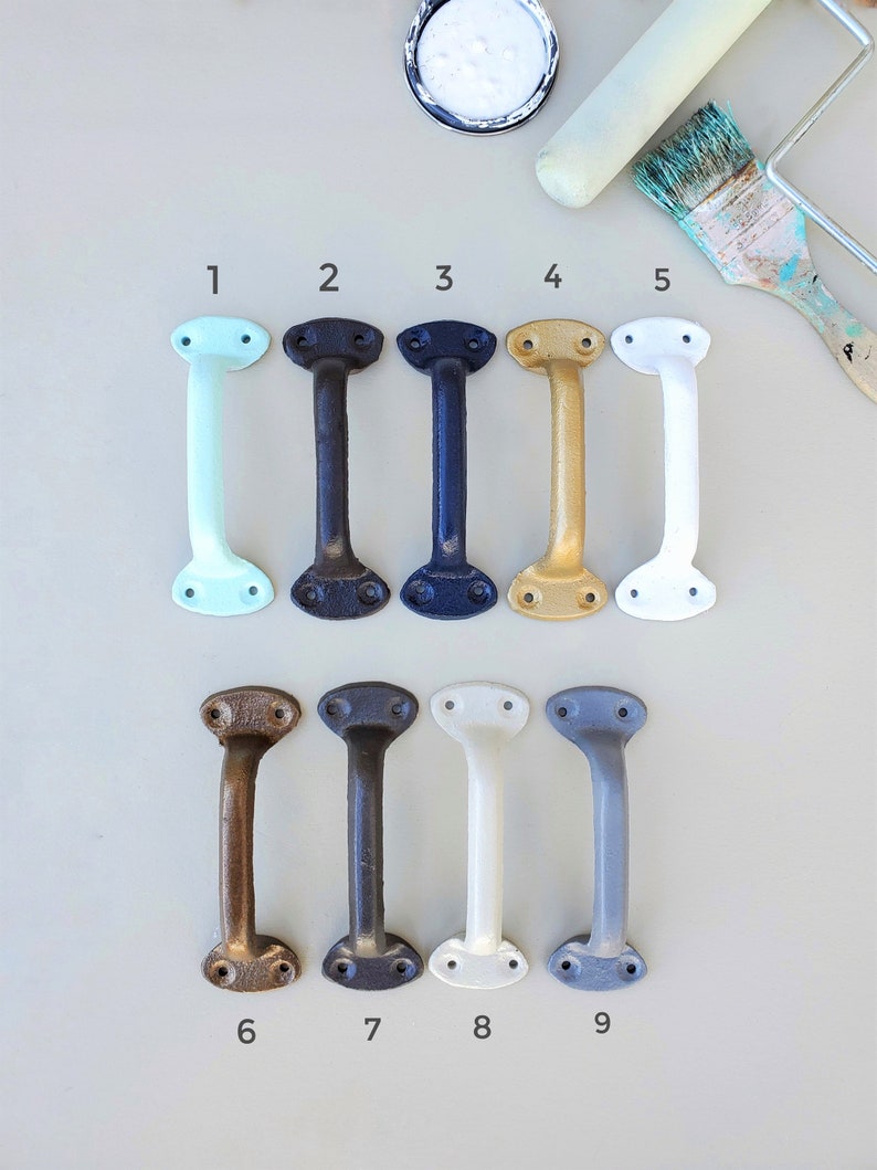 Op de afbeelding: Negen verschillende gekleurde kastgrepen of -knoppen. De grepen zijn van metaal en hebben een eenvoudig, klassiek ontwerp. De kleuren zijn: lichtblauw, bruin, zwart, goud, wit, brons, donkerbruin, cr&egrave;mewit en grijs.