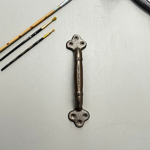 Könnte beinhalten: Ein rustikaler, dunkelbrauner Türknauf aus Metall mit einem dekorativen, vierblättrigen Design. Der Knauf hat eine glatte, leicht strukturierte Oberfläche.