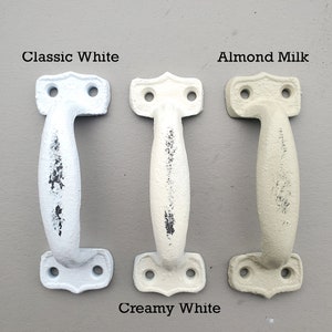 Op de afbeelding: Drie deurgrepen van gietijzer in verschillende tinten wit. De grepen zijn gelabeld met "Classic White", "Creamy White" en "Almond Milk".